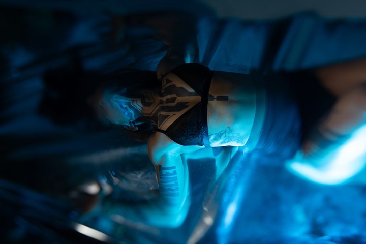 A figure on a reflective floor under deep cobalt light, the mirrored surface rippling the blue back across the frame.