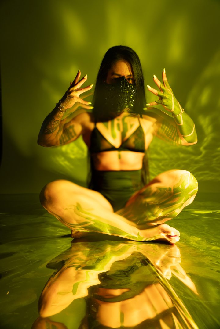 A cross-legged figure in cool blue and green strobe, hands raised, the gelled light dividing warm and cool across the frame.