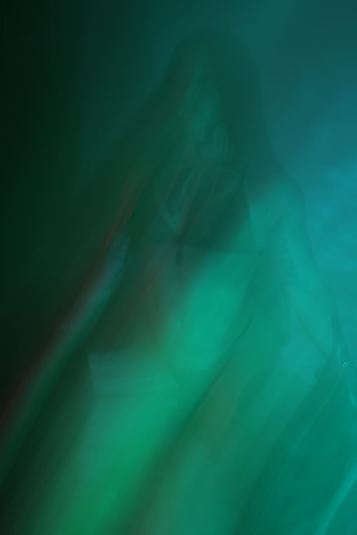 A near-abstract figure dissolved into green and teal by long-exposure motion blur, the body barely emerging from the wash.