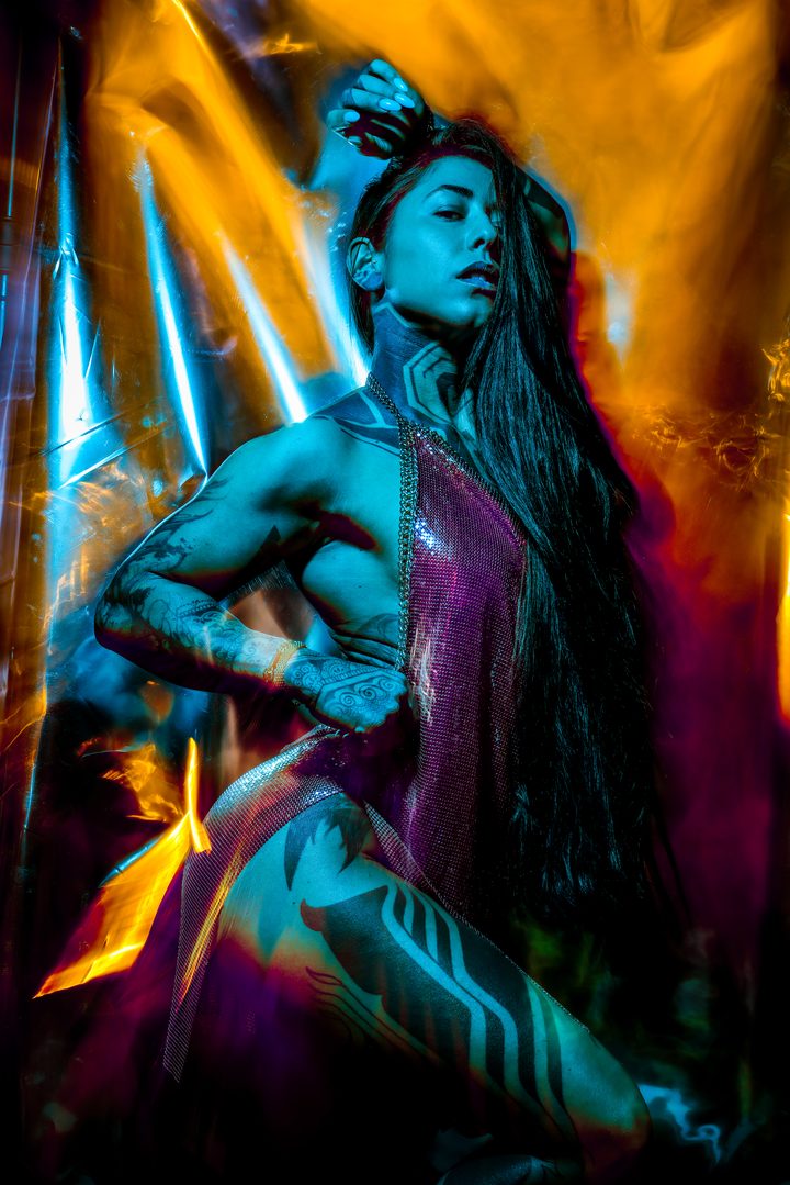 A standing figure lit by amber and blue, reflective sheeting around the body throwing the color back like flame.