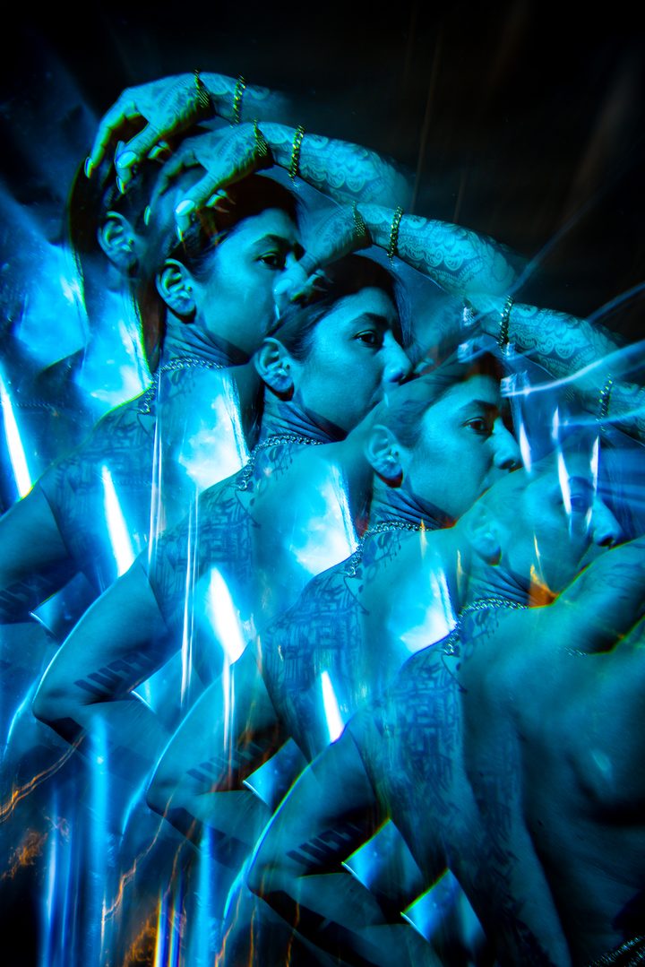 A figure held in blue and amber light among reflective sheeting, the warm and cool gels meeting across the body.