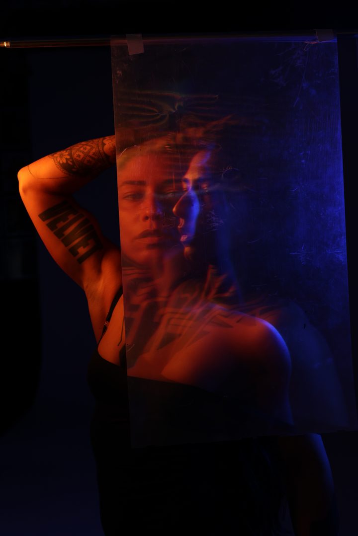 A figure under projected light in green and blue, the body ghosted and doubled by a long exposure against the grid.