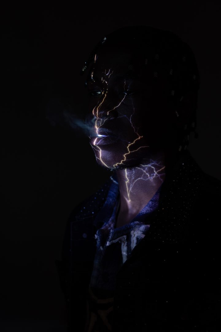 Lightning projected across a man's face and neck, sculpted from near-black, a companion to the teal projection study.
